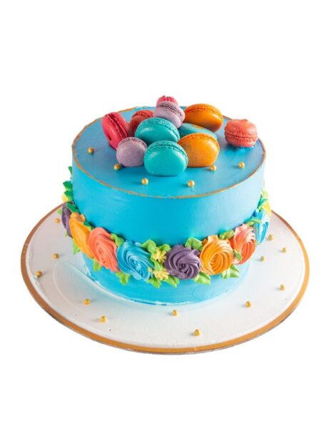 Blue cake decorated with colorful buttercream flowers and topped with assorted macarons.