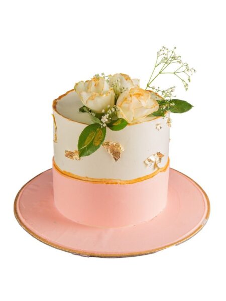 Elegant fresh floral cake with white and pink tiers, golden accents, and cream roses on top.