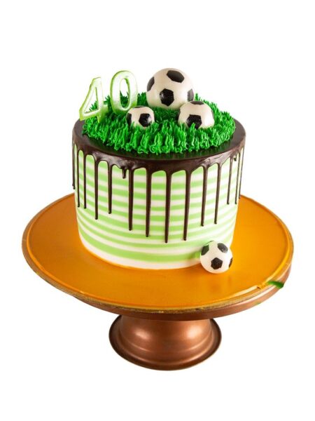 Football theme cake with striped design, chocolate drip, green grass, and fondant soccer balls.