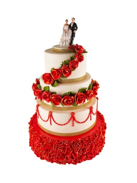 Three-tier wedding cake with red roses, golden accents, ruffled base, and bride-and-groom topper.